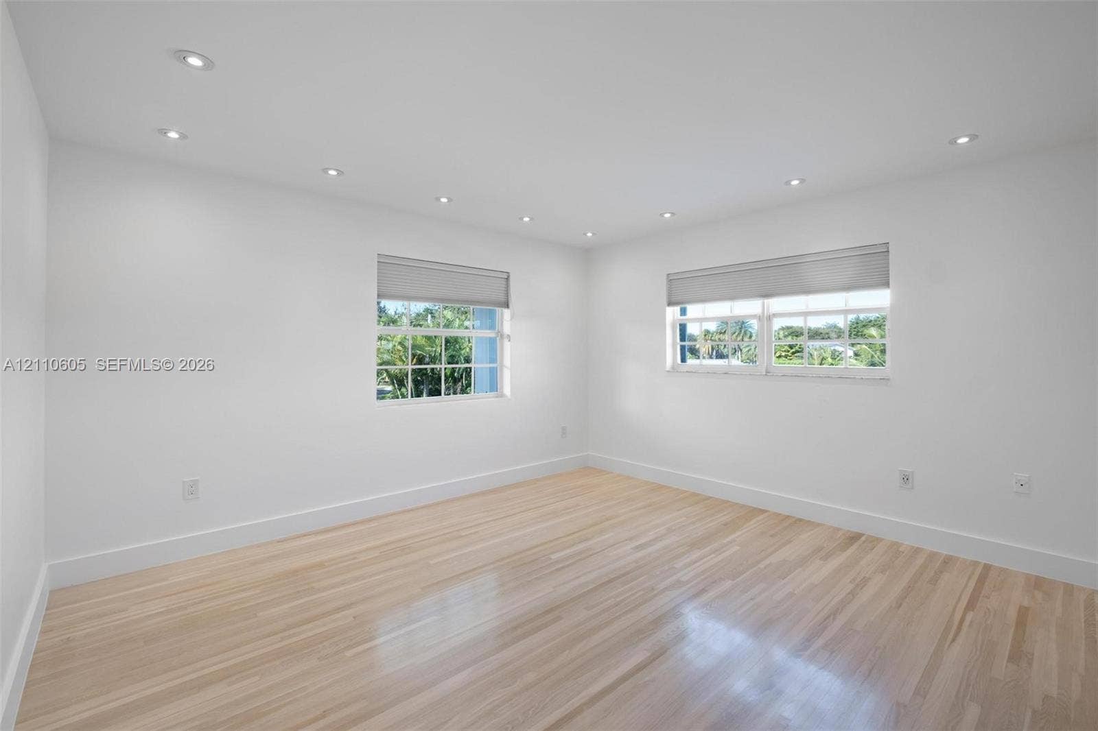 Neutral-toned room featuring light wood-finish flooring, recessed ceiling lighting, and multi-pane windows with integrated blinds