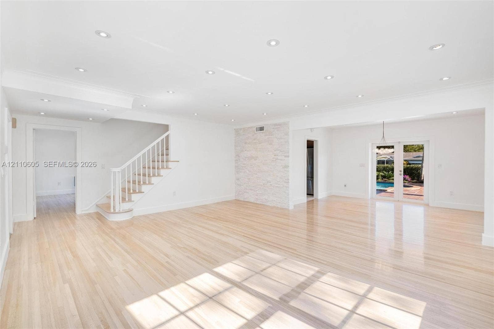 Open-concept interior featuring light wood-finish flooring, recessed lighting, a stone-accented wall, and white staircase railing