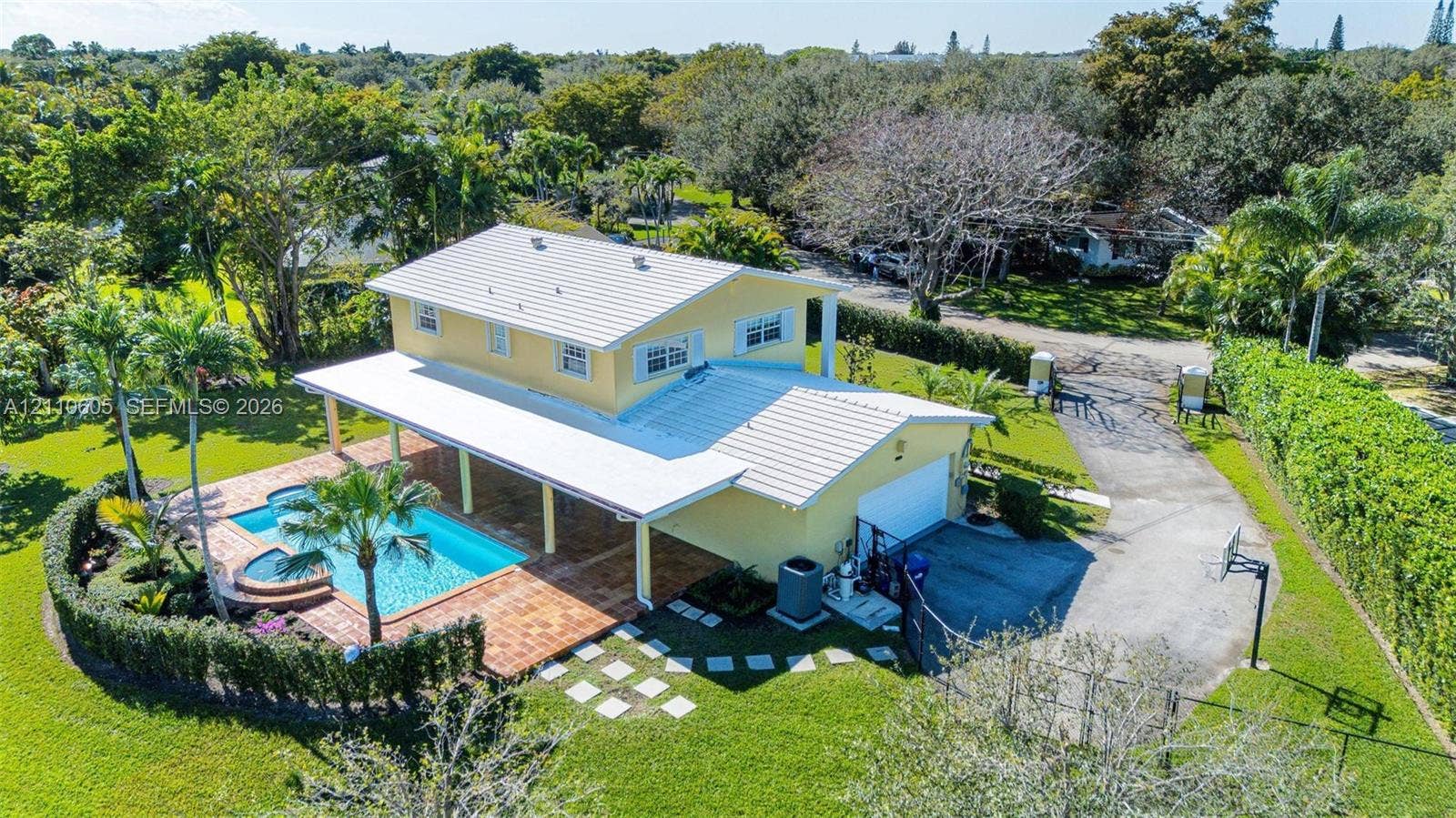 Two-story residence featuring a metal roof, an expansive covered patio, a tiled pool with an integrated spa, and a paved driveway situated on a large, landscaped lot