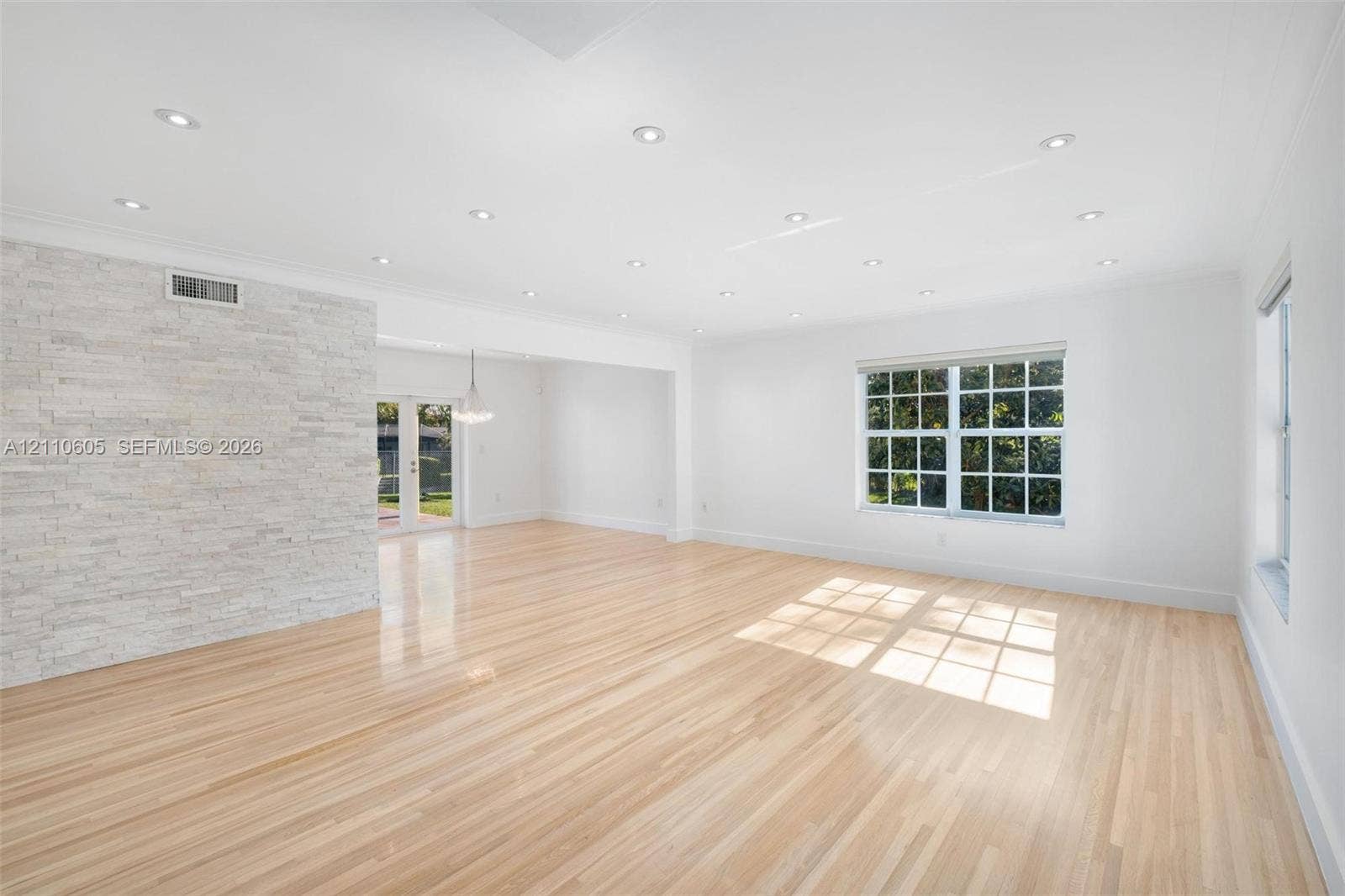 Light-toned wood flooring, textured stone accent wall, recessed ceiling lighting, and multi-pane grid windows