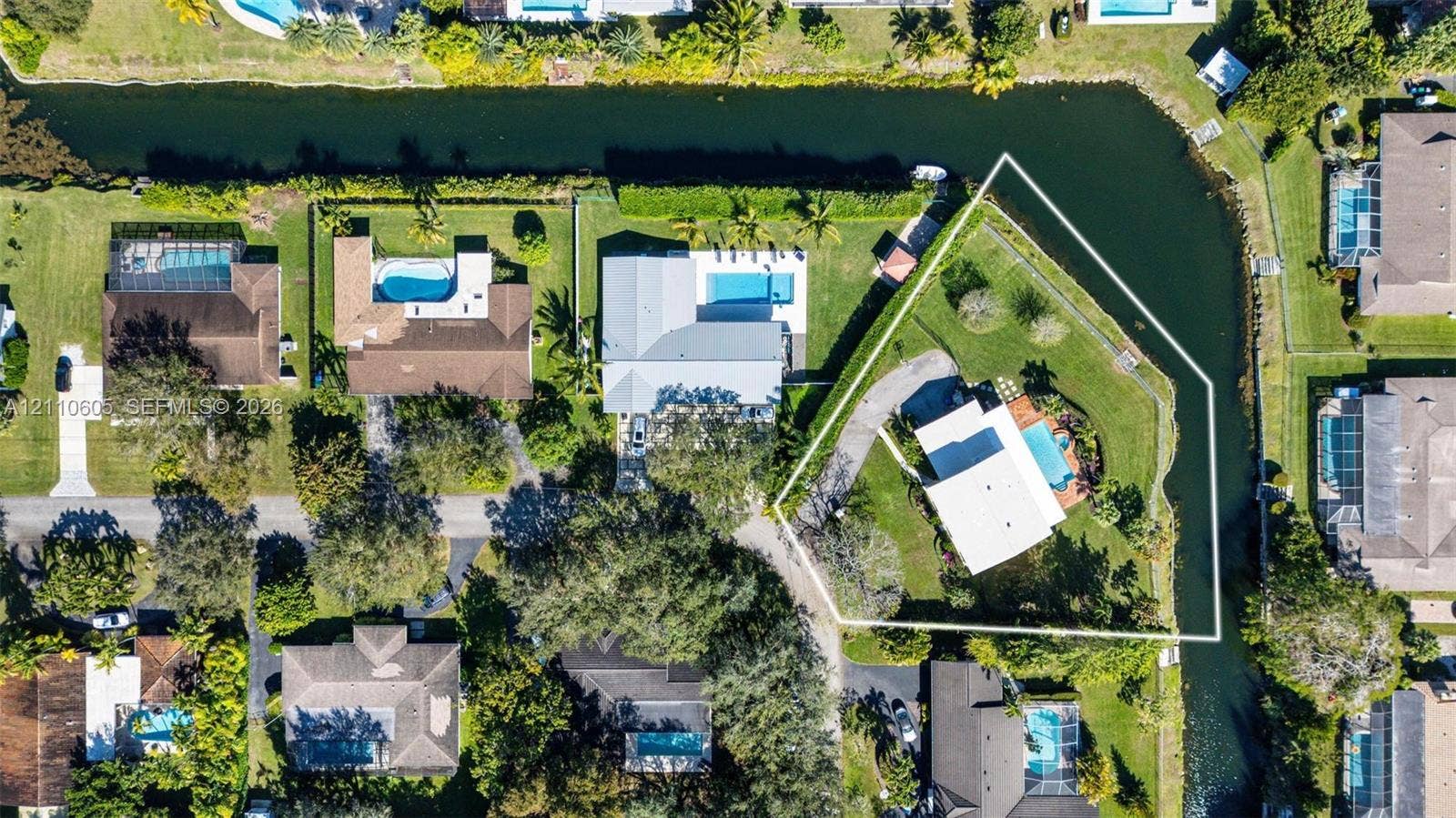 Aerial perspective of a waterfront lot featuring extensive canal frontage, an in-ground swimming pool, a paved driveway, and mature landscaping