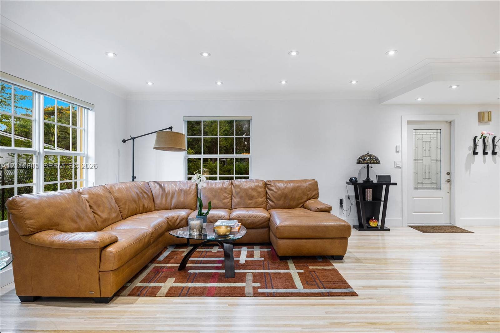 Living area featuring light-toned wood-finish flooring, recessed lighting, multi-pane windows, and a glass-paneled entry door