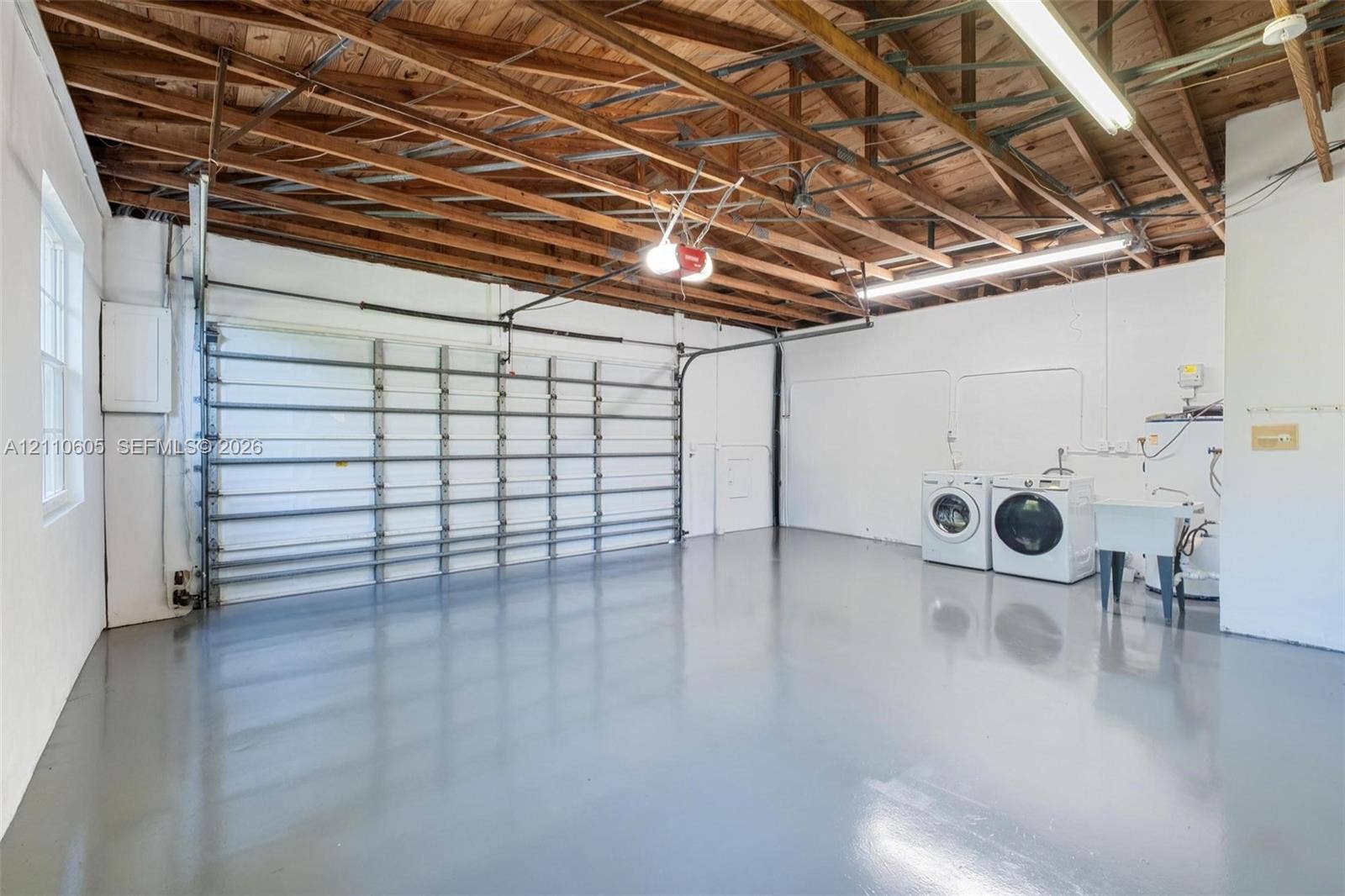 Multi-vehicle garage featuring an exposed wood-beam ceiling, finished epoxy flooring, a sectional roll-up door, and a built-in utility sink