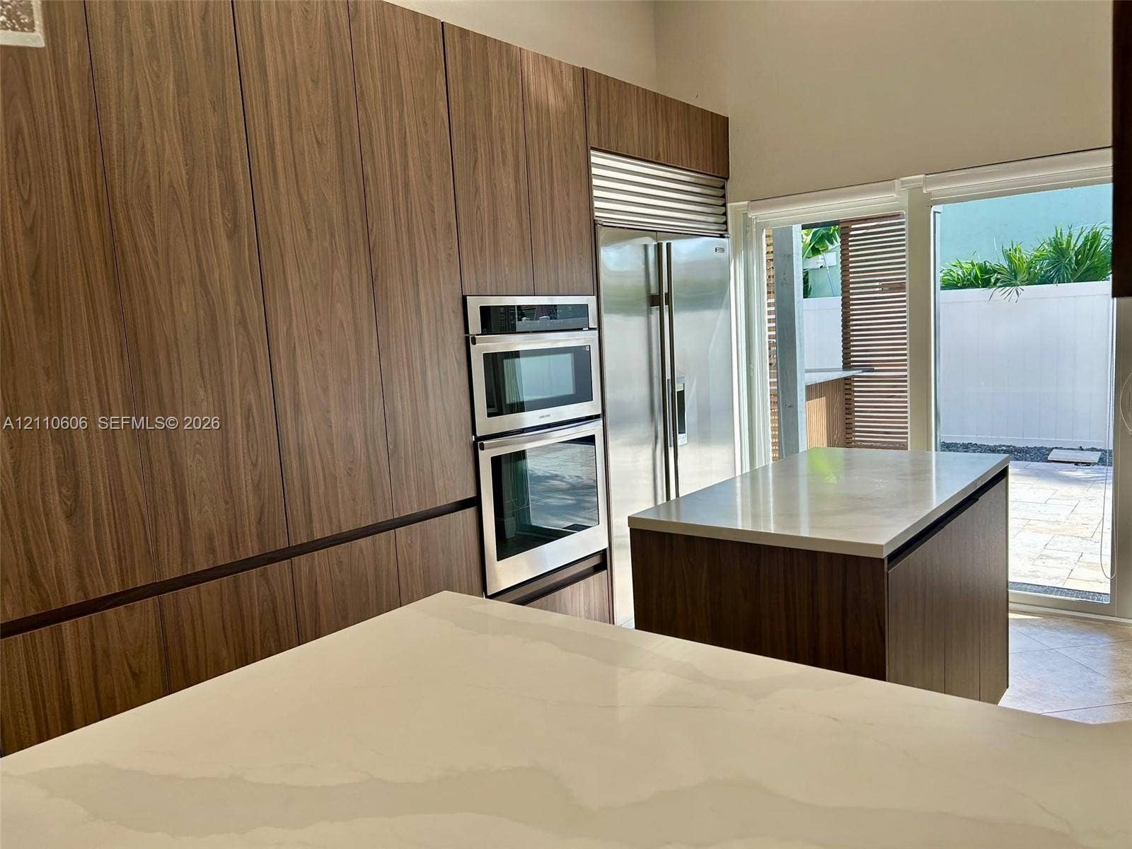 Modern kitchen featuring full-height wood-grain cabinetry, quartz countertops, a dual wall oven, and stainless steel refrigerator