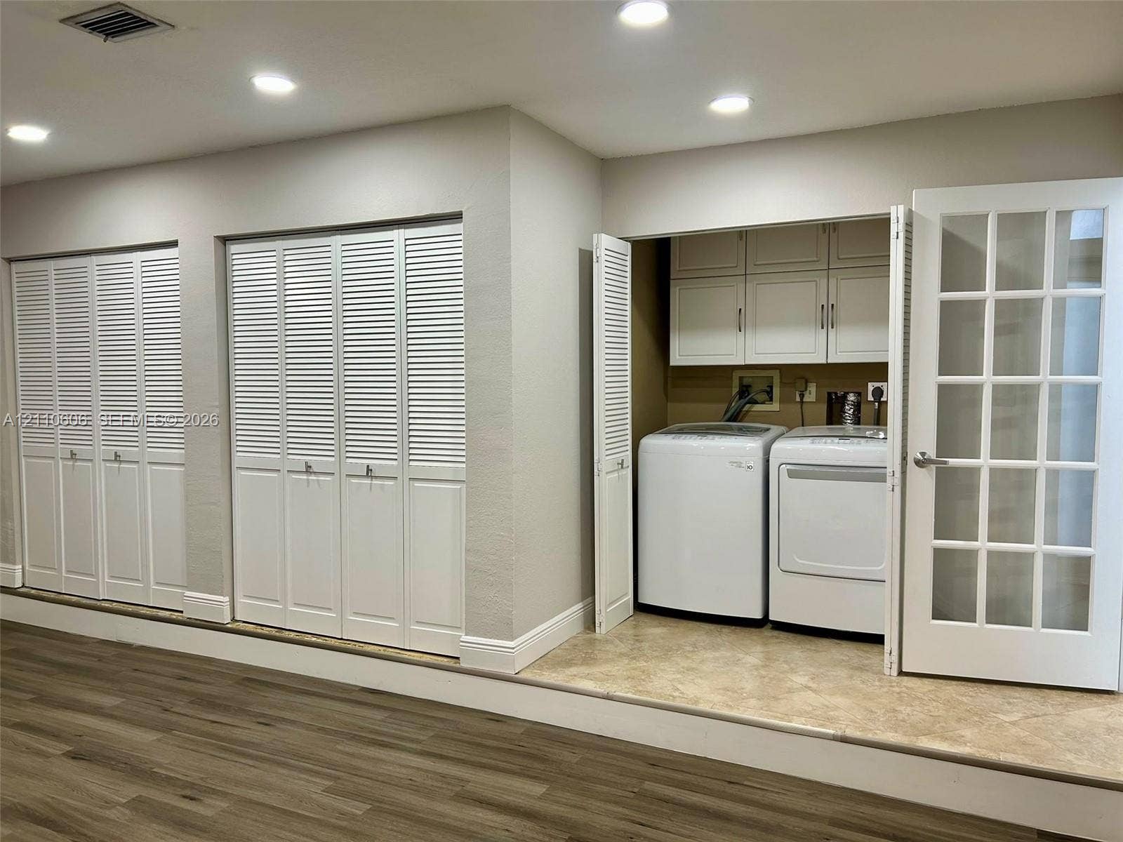 Laundry area featuring built-in cabinetry, recessed lighting, and louvered closet doors, set on a raised tile platform with wood-finish flooring in the surrounding space