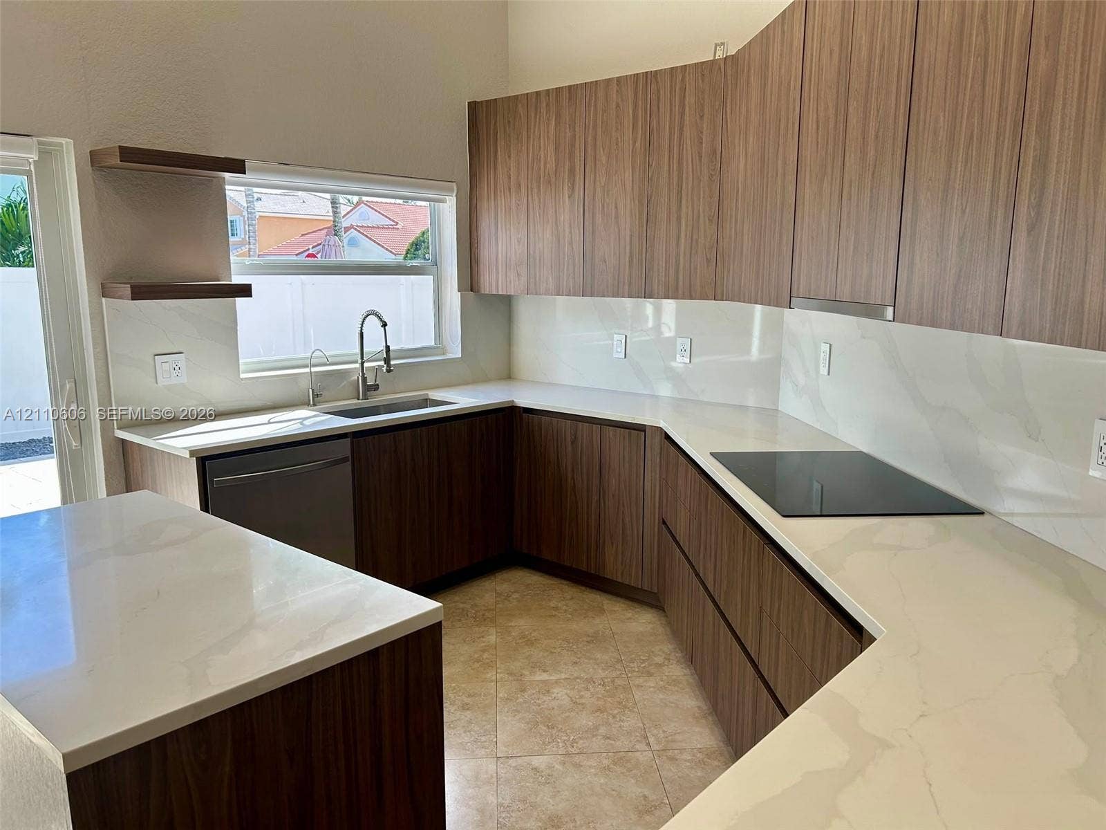 Kitchen featuring wood-finish cabinetry, stone-style countertops, integrated cooktop, stainless steel sink with gooseneck faucet, and floating shelves
