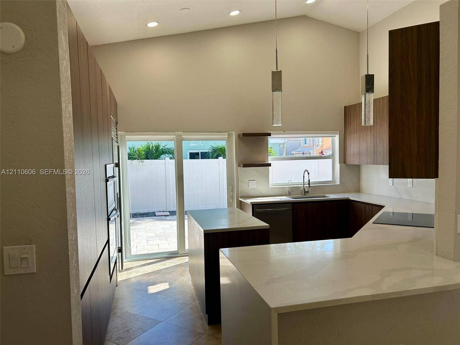 Kitchen featuring flat-panel cabinetry, stone-finish countertops, stainless steel appliances, vaulted ceilings, and pendant lighting