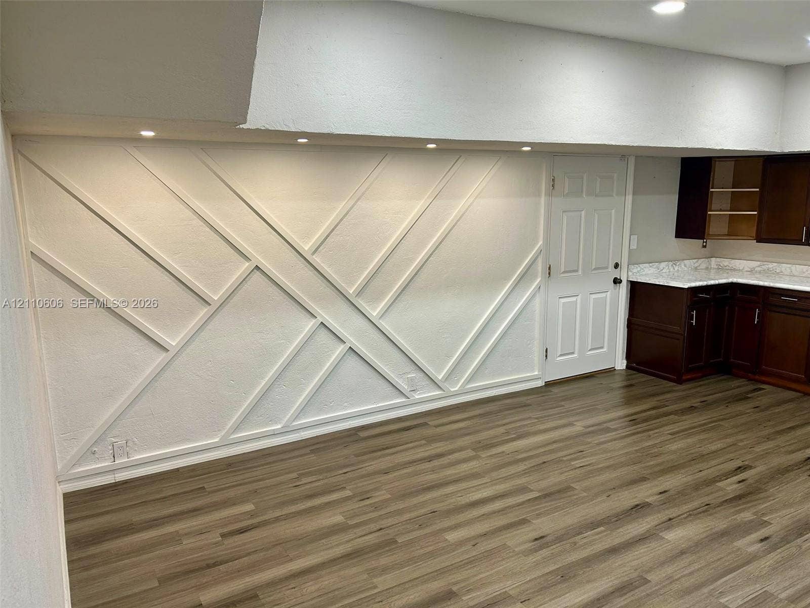 Geometric wall molding, wood-finish flooring, recessed ceiling lighting, and dark-toned cabinetry with stone-finish countertops