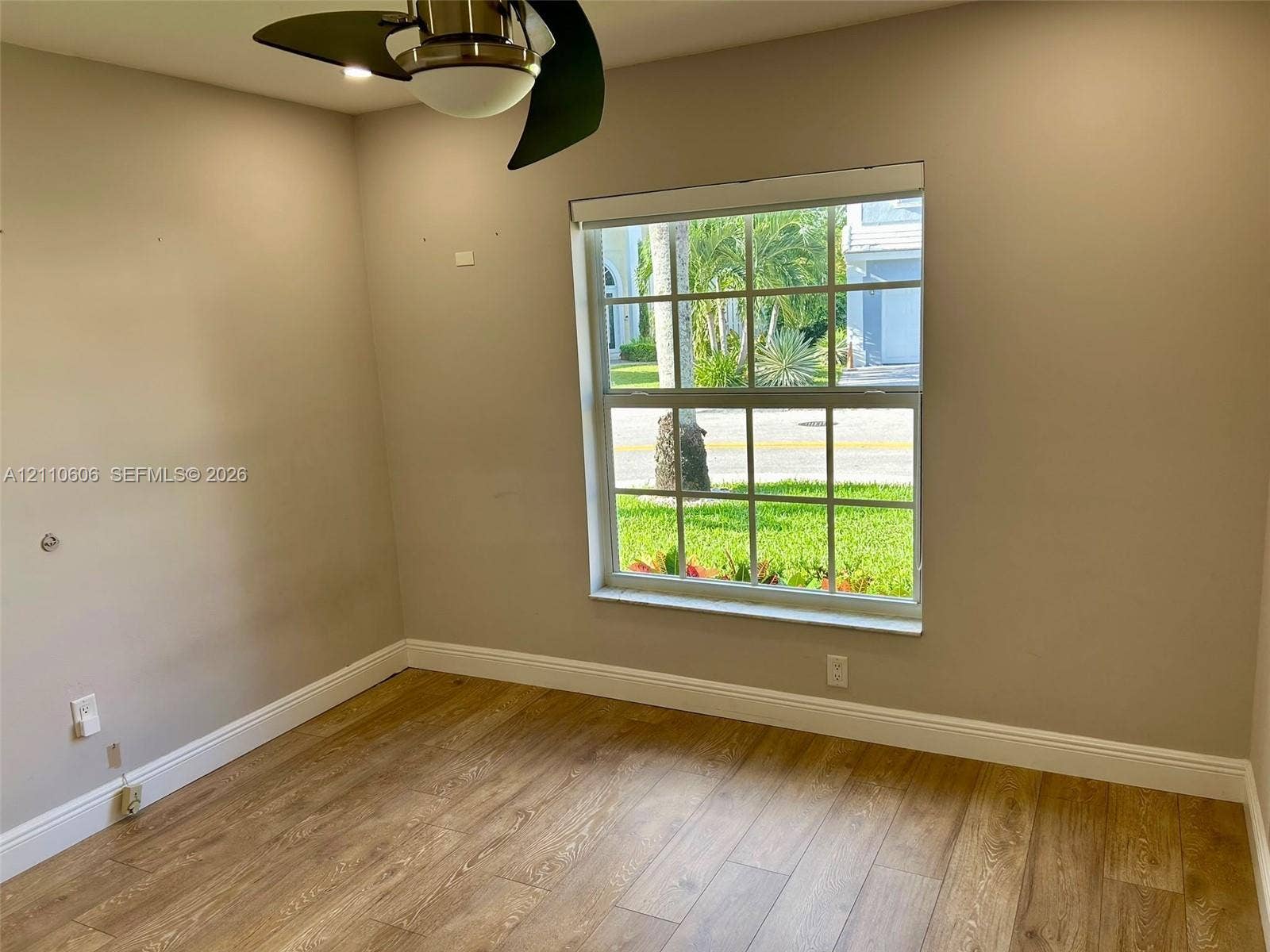 Neutral interior space featuring wood-finish flooring, a multi-pane window with a muntin grid, and an attached ceiling fan with integrated lighting