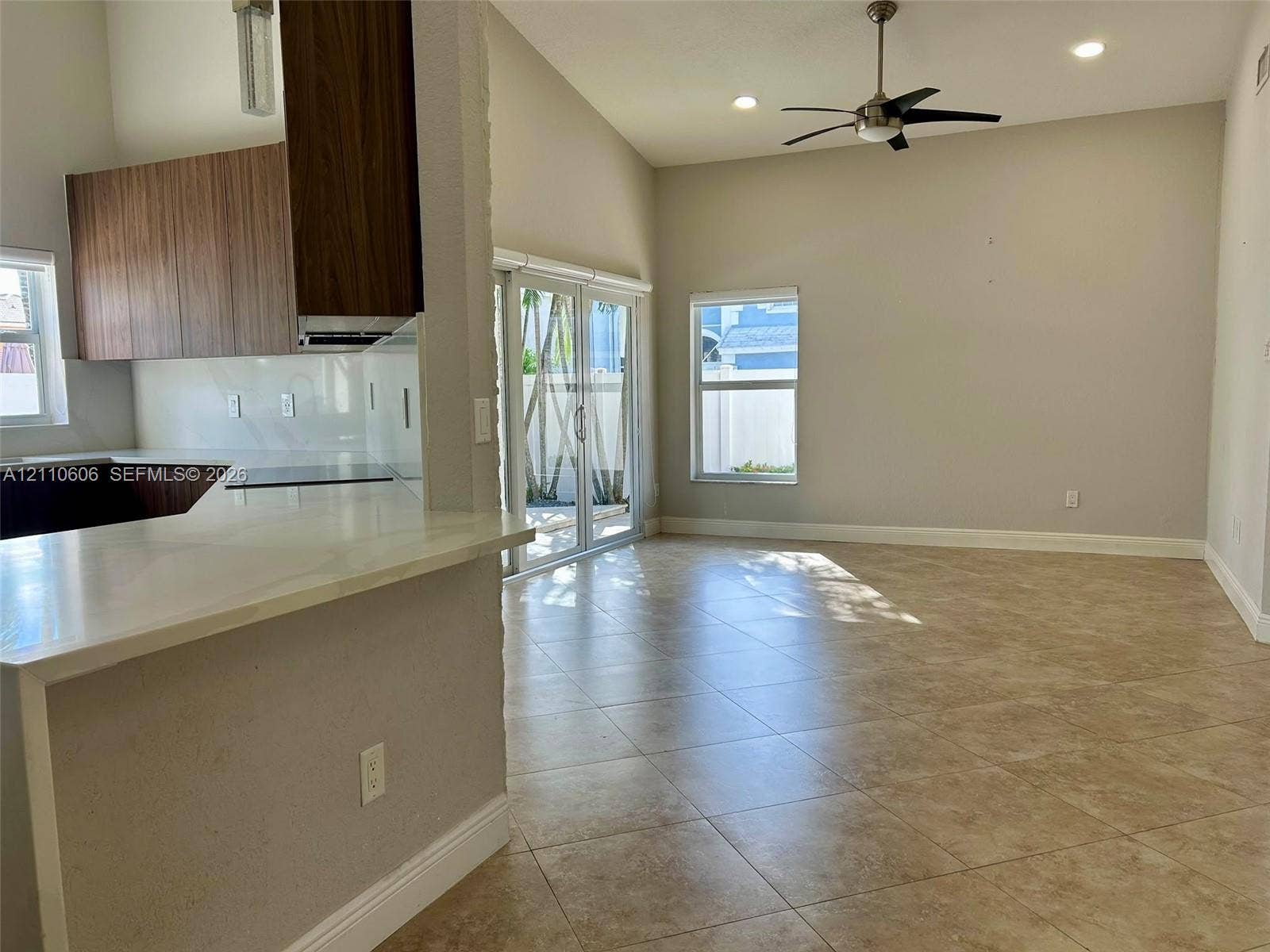 Open-concept interior featuring vaulted ceilings, neutral tile flooring, wood-finish cabinetry, white solid-surface countertops, and sliding glass doors