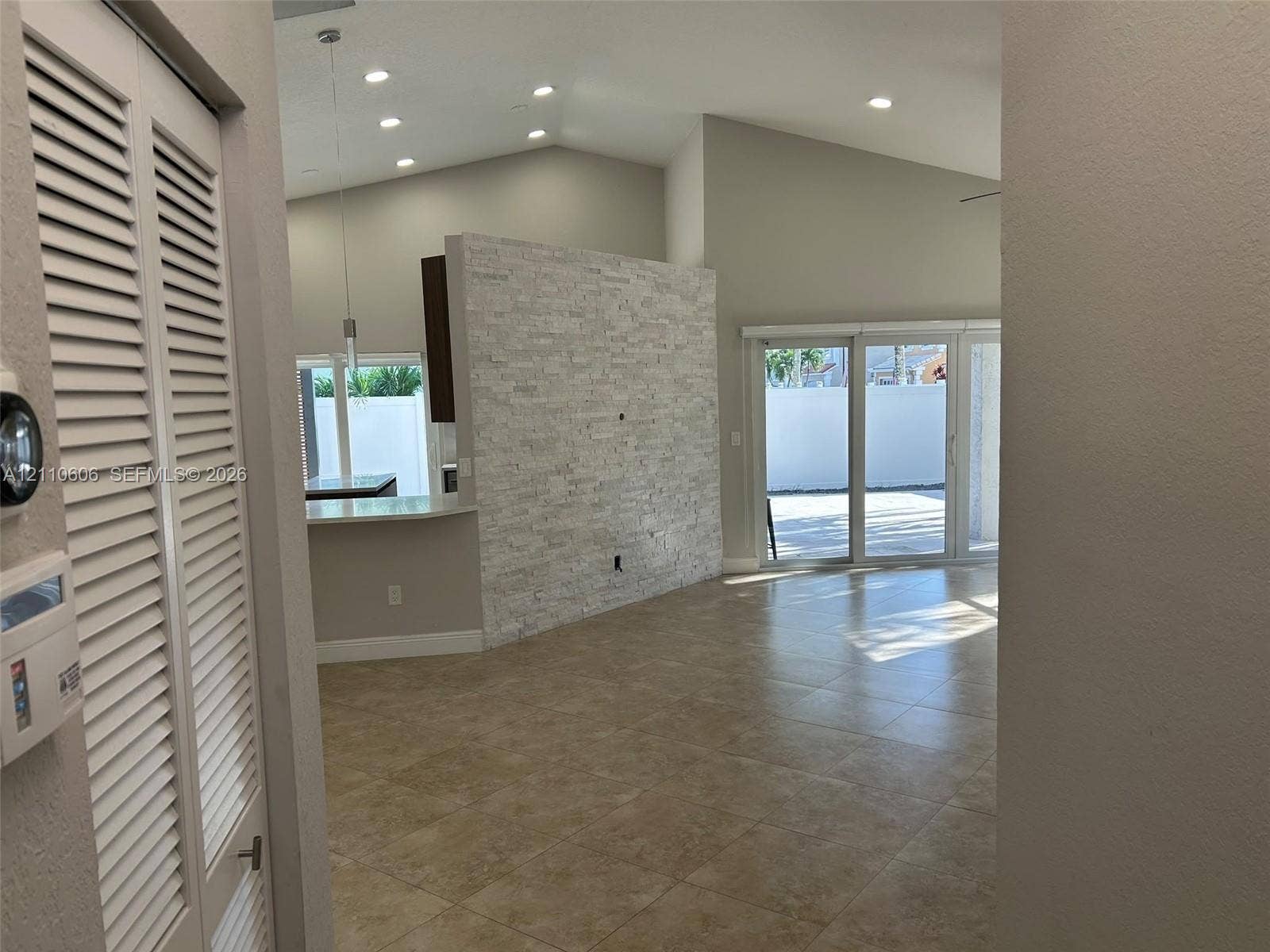 Vaulted ceilings featuring recessed lighting, a stone-finish accent wall, and large-format tile flooring, complemented by sliding glass doors leading to the exterior