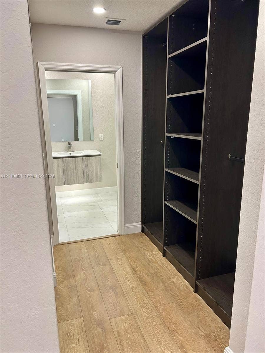 Custom dark-finish built-in shelving, wood-finish flooring, floating vanity with a rectangular sink, wall-mounted faucet, and polished large-format tile flooring