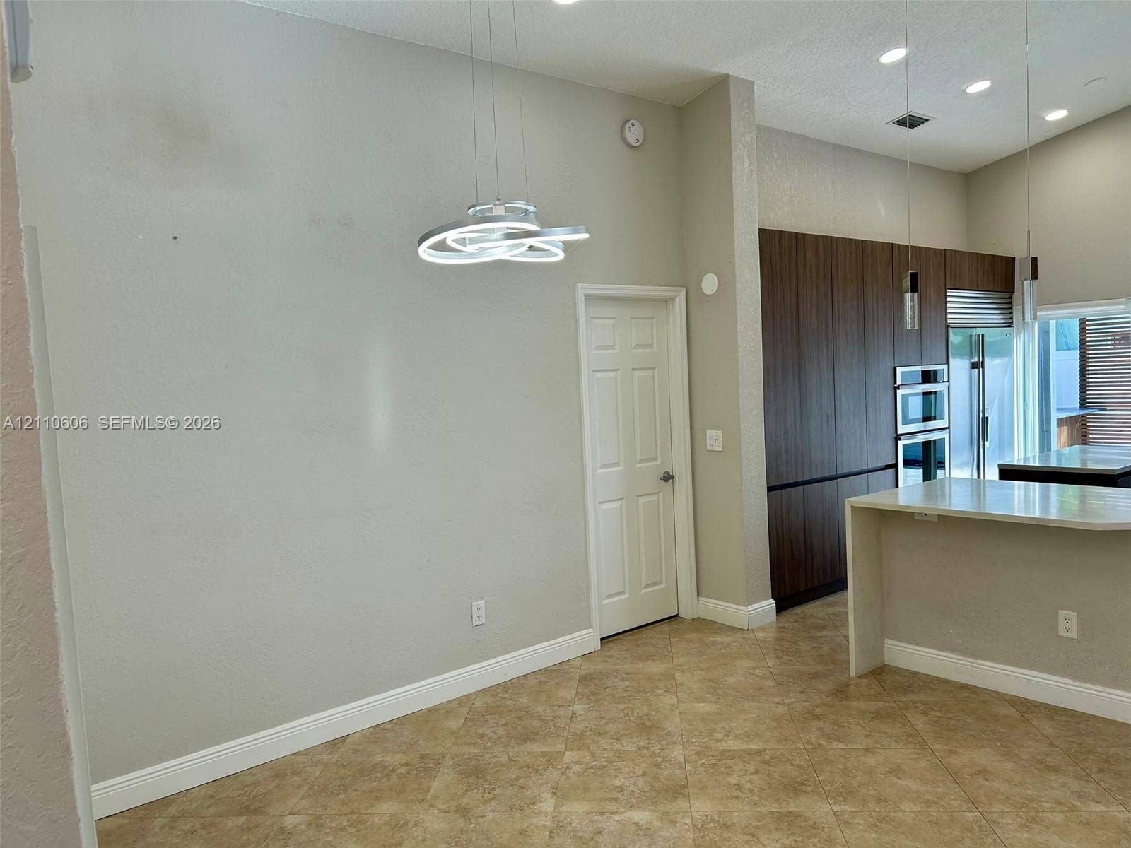 Vaulted ceilings featuring modern sculptural pendant lighting, stone-finish tile flooring, floor-to-ceiling wood-finish cabinetry, and recessed lighting