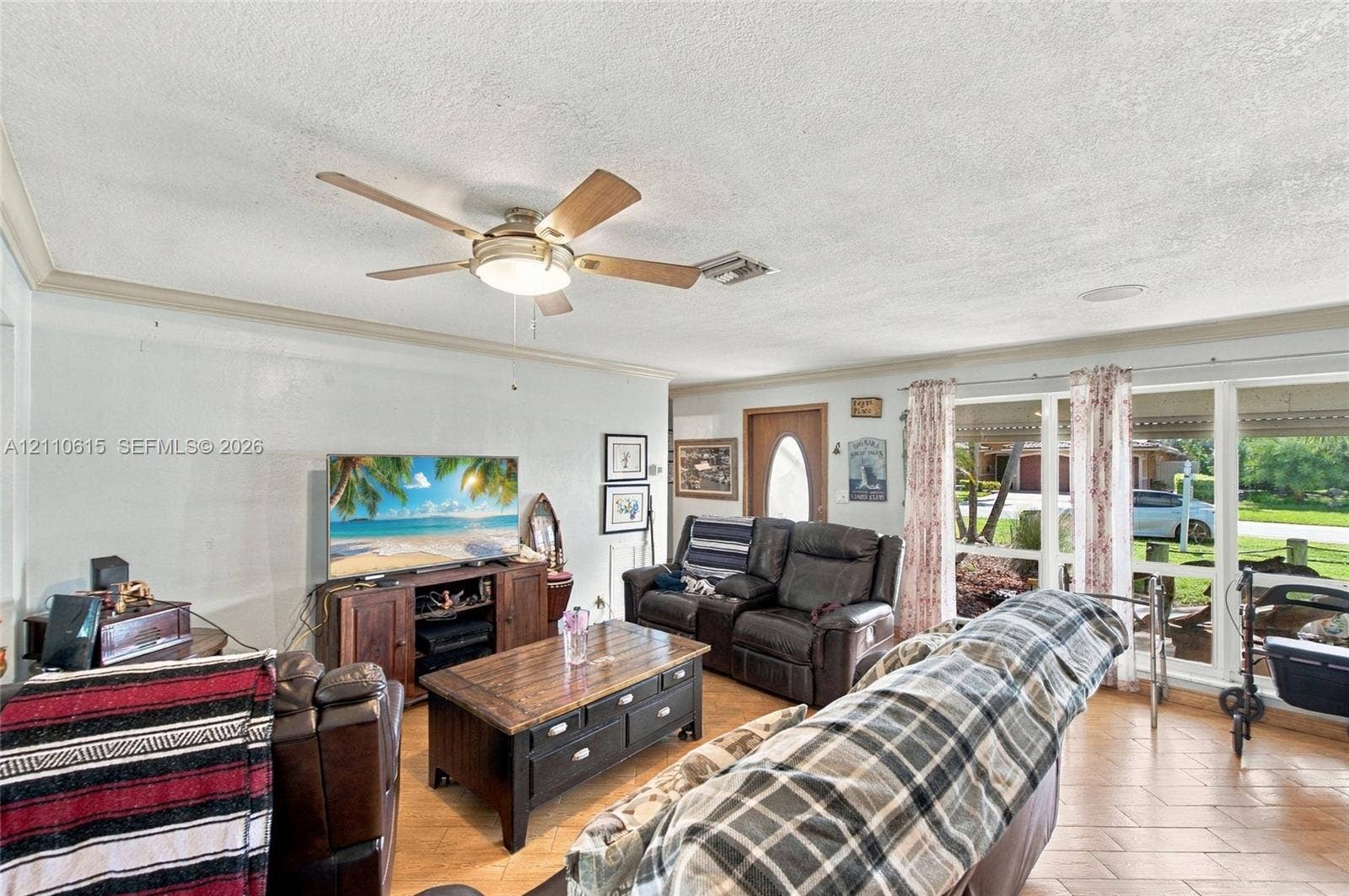 Open-concept interior featuring light-toned tile flooring, a multi-blade ceiling fan with integrated lighting, and expansive windows providing natural illumination