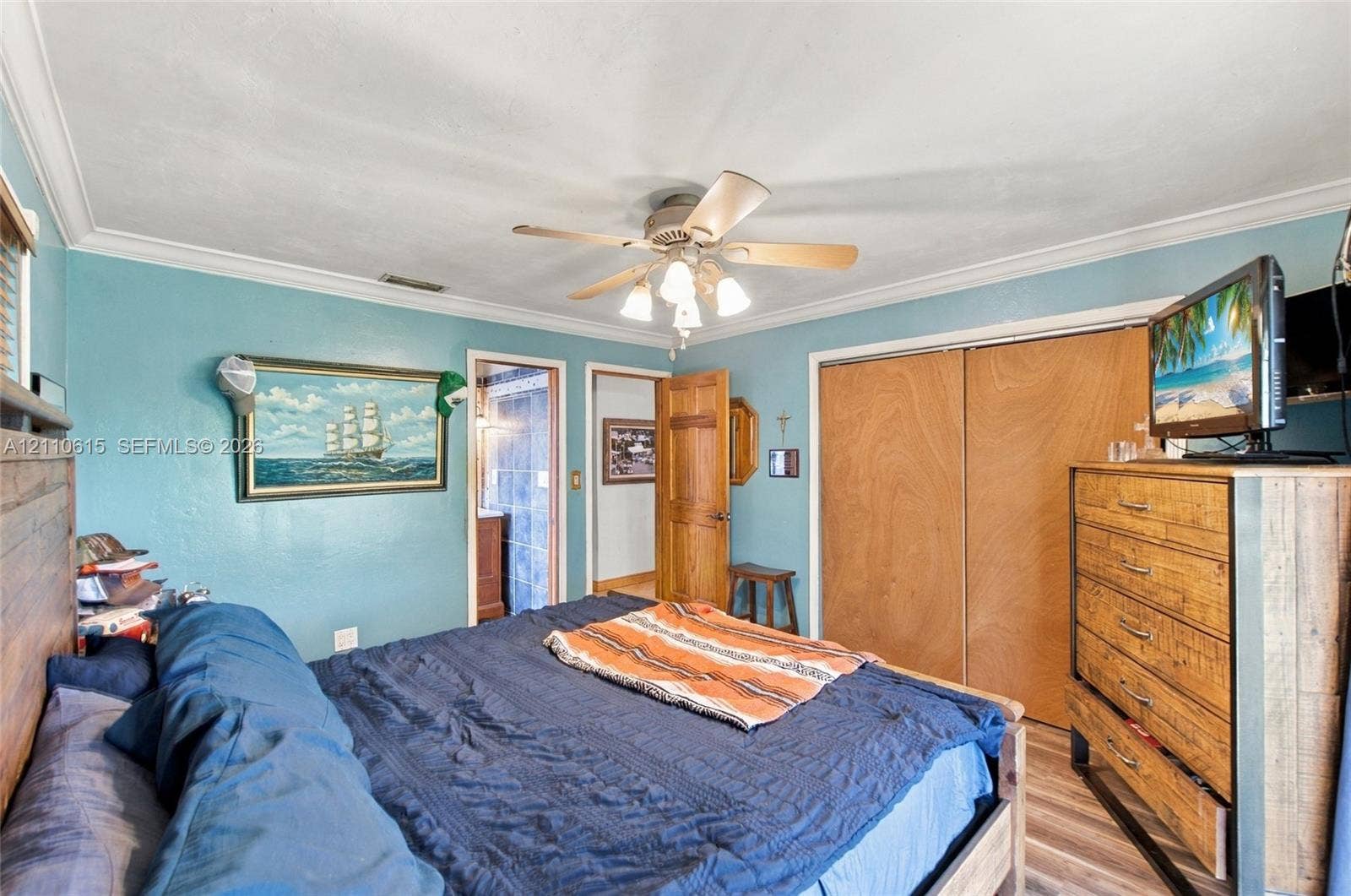 Bedroom featuring wood-finish flooring, a ceiling fan with integrated lighting, crown molding, and wooden sliding closet doors