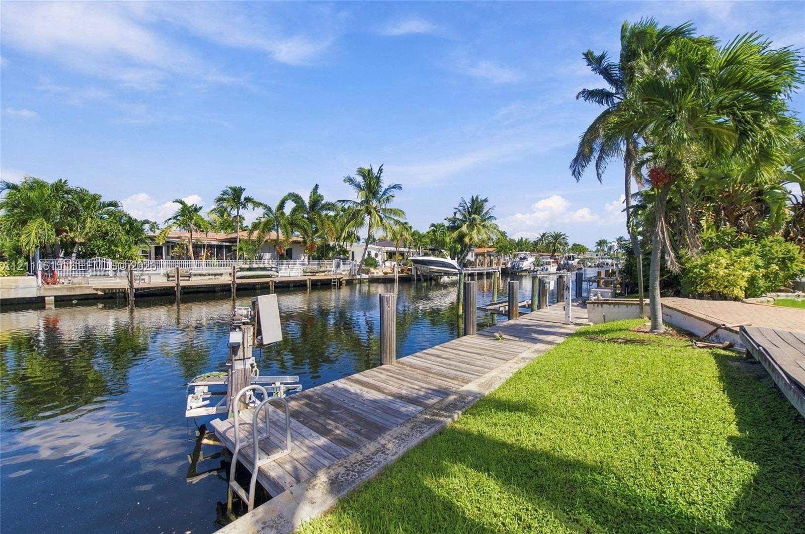Waterfront property featuring a wooden boat dock, boat lift, manicured lawn, and mature palm trees