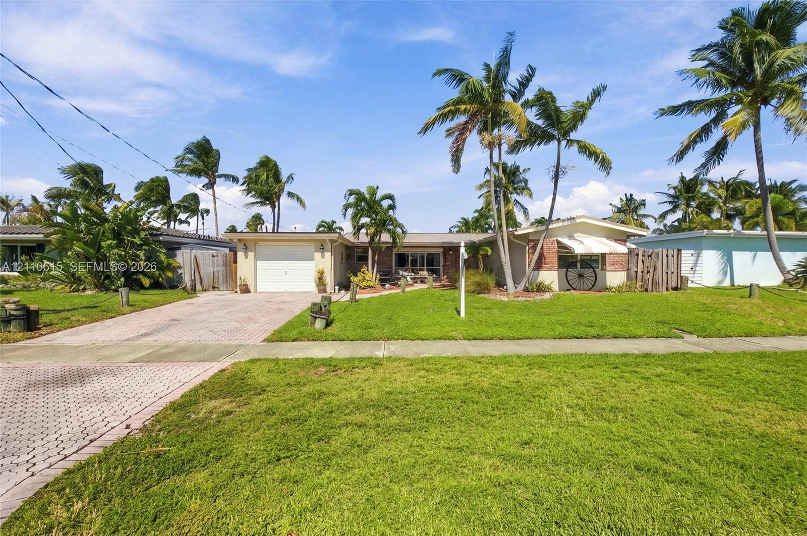 Single-story exterior featuring a brick facade, paved driveway, one-car garage, and established palm trees