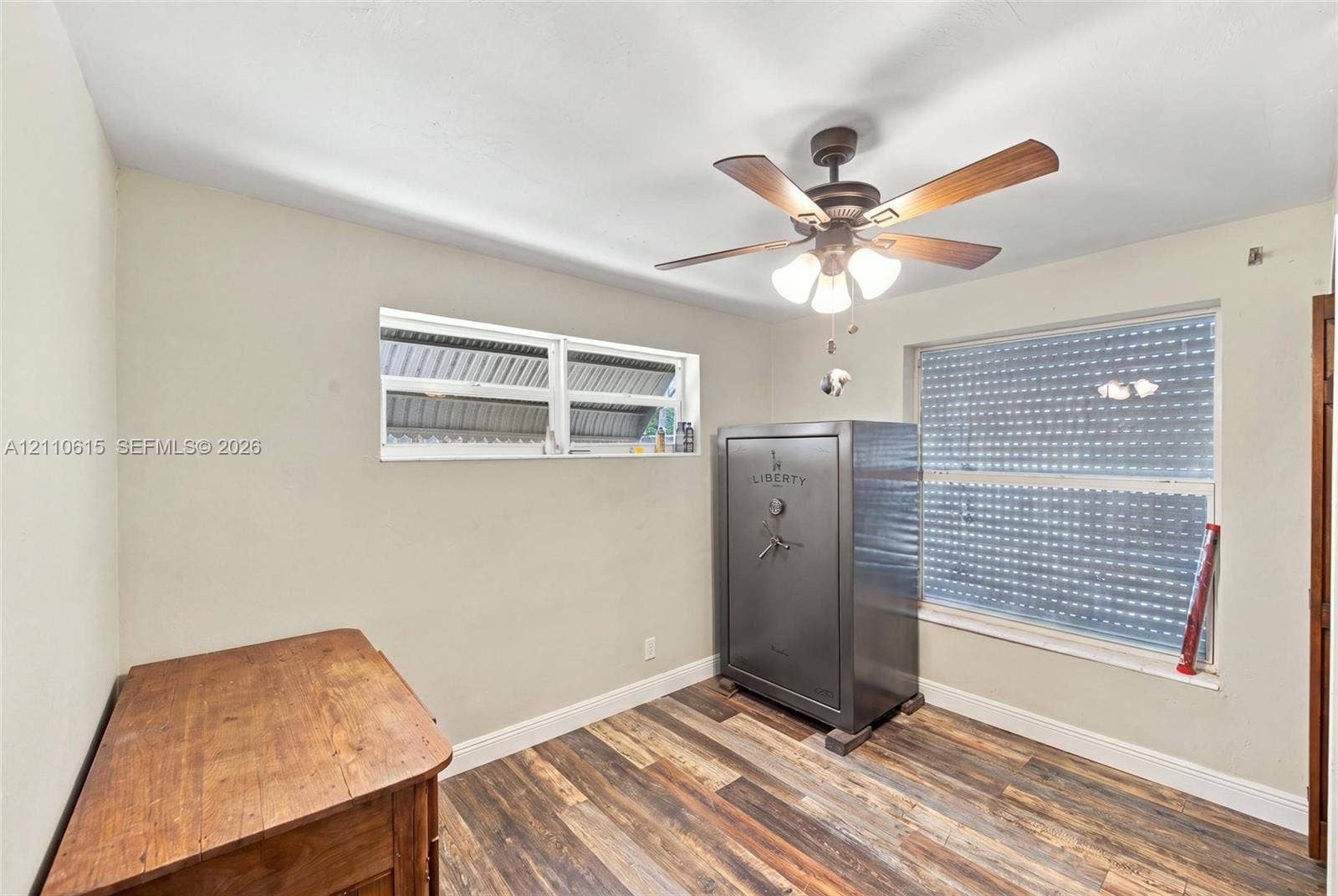 Wood-finish flooring, dual windows with exterior security shutters, and a ceiling fan with integrated lighting