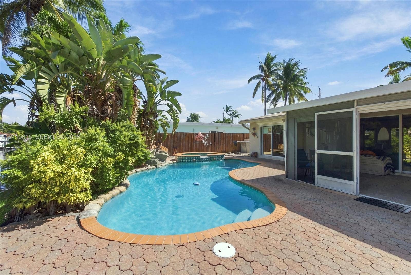 Freeform swimming pool with integrated spa, concrete paver patio, screened lanai, and wood perimeter fencing