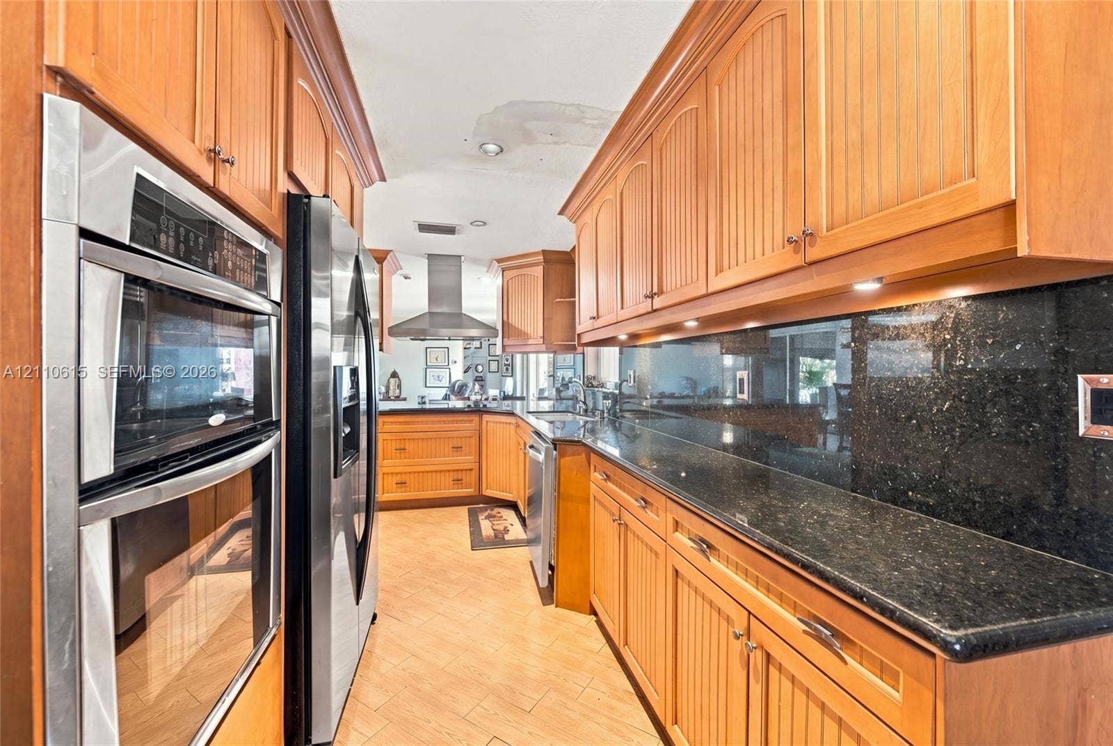 Kitchen featuring wood cabinetry with beadboard detailing, dark stone countertops, stainless steel wall-mounted double oven, stainless steel refrigerator, and metal range hood