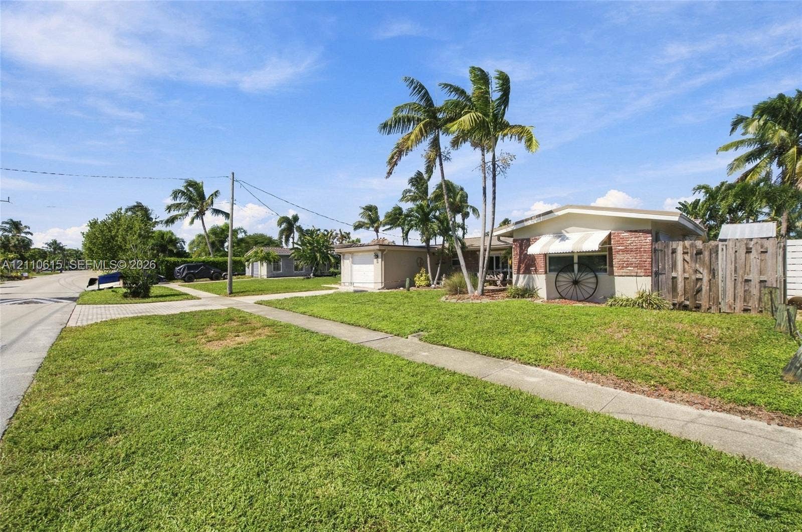 Single-story residence featuring brick facade detailing, an attached garage, striped window awnings, and mature palm trees