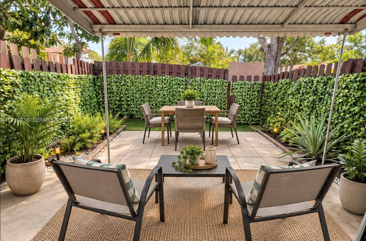 Covered patio featuring large-format concrete pavers, a privacy fence with integrated artificial greenery, and low-voltage landscape lighting
