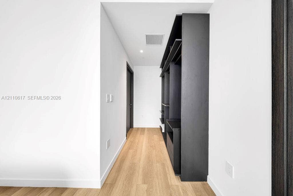 Hallway featuring wood-finish flooring, recessed ceiling lighting, and built-in dark cabinetry with open shelving