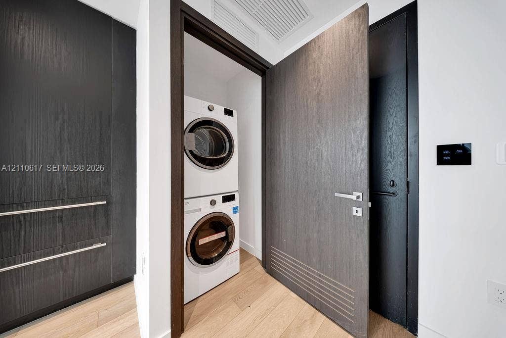 Laundry area featuring a stackable washer and dryer, wood-finish flooring, custom dark-toned cabinetry, and minimalist doors with linear detailing