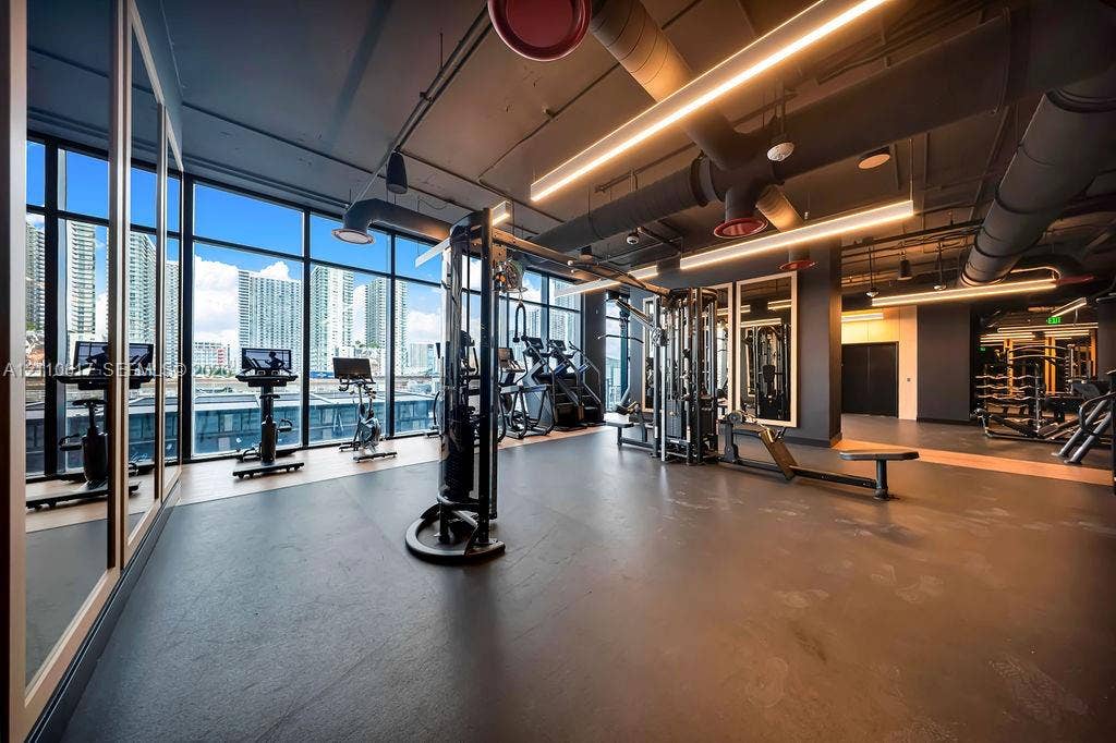 Fitness center featuring floor-to-ceiling windows, industrial-style exposed ductwork, recessed linear lighting, and wall-to-wall mirrors