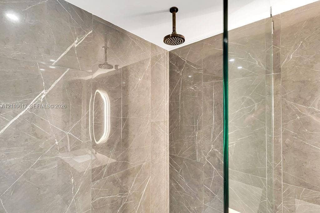 Walk-in shower featuring floor-to-ceiling stone-patterned tile, ceiling-mounted rainfall shower head, and glass enclosure