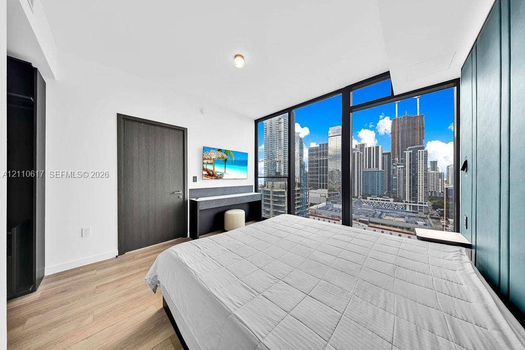 Floor-to-ceiling windows featuring urban skyline scenery, wood-finish flooring, custom teal-paneled accent wall, and built-in dark-toned cabinetry