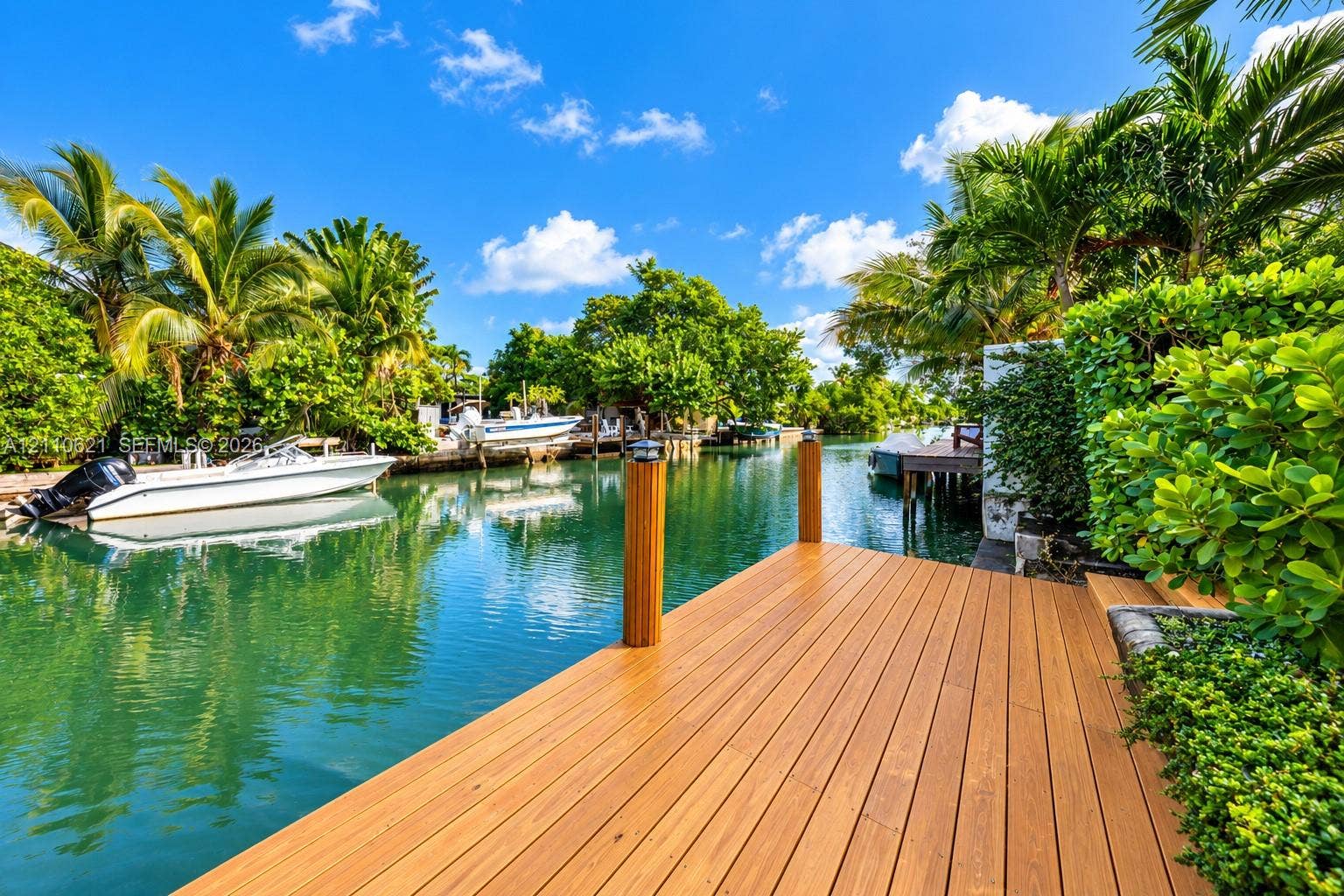 Waterfront dock featuring composite decking, wooden pilings with solar caps, and mature tropical landscaping