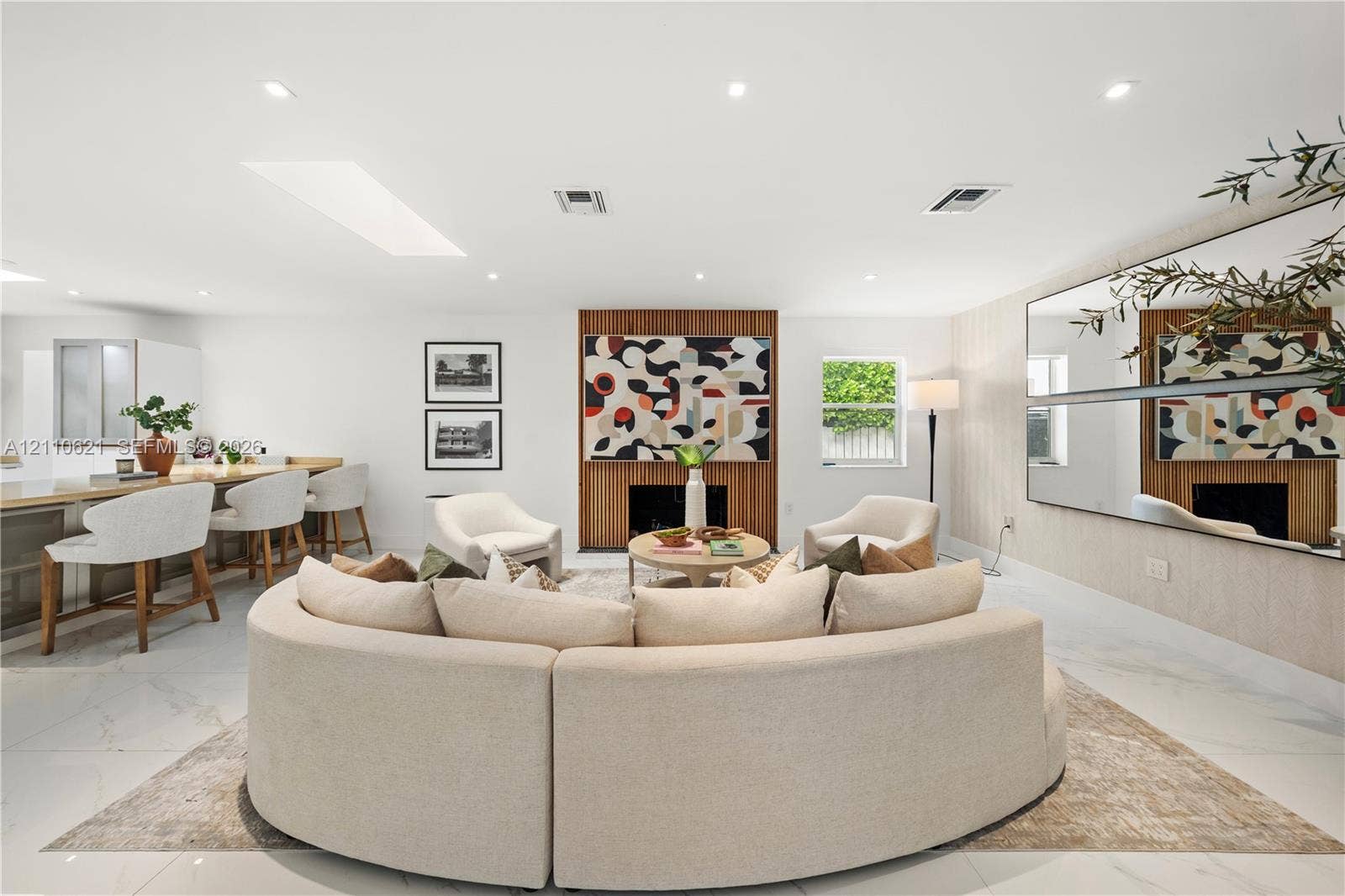 Open-concept living space featuring large-format tile flooring, a recessed skylight, recessed lighting, a wood-paneled fireplace surround, and extensive wall-mounted mirrors