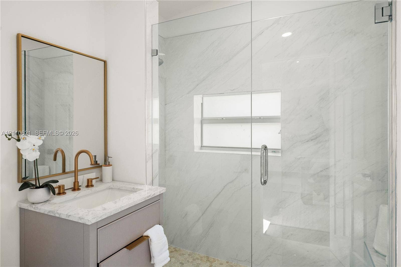 Modern vanity with stone-look countertop, brass-finish faucet, and framed mirror