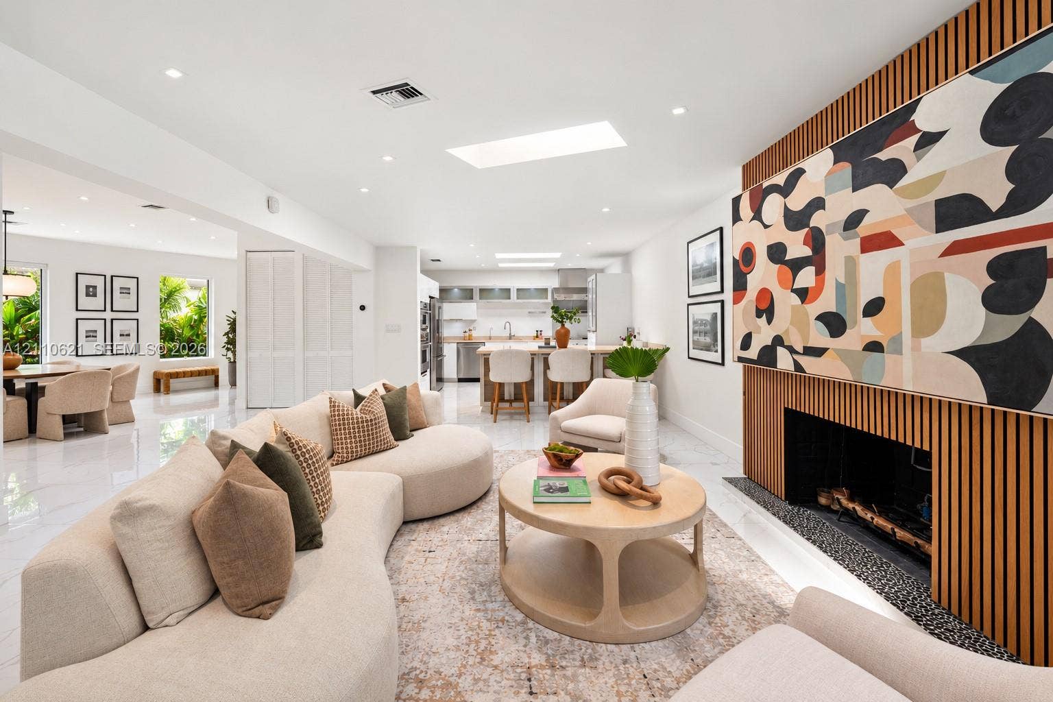 Open-concept living space featuring white stone-finish flooring, two skylights, recessed lighting, and a linear fireplace with floor-to-ceiling wood-slat paneling