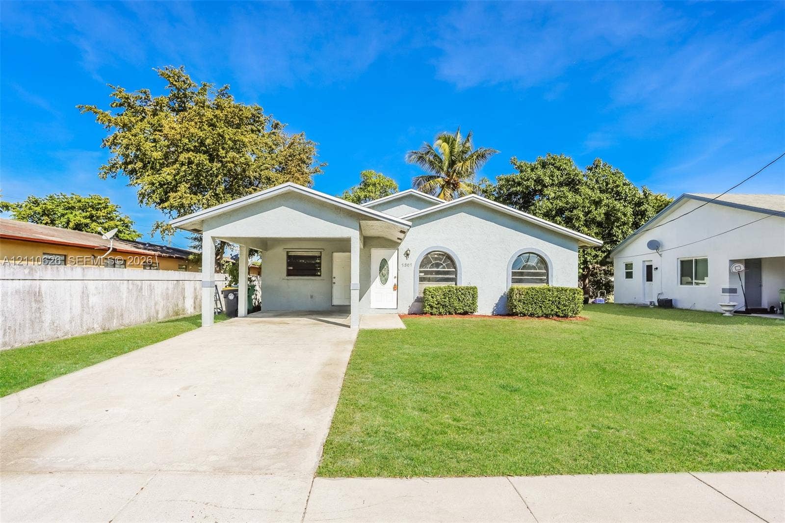 1301 NW 2nd Street, Dania, Dania Beach, FL 33004 Single-story exterior featuring a light-toned stucco facade, arched windows, covered carport, and a manicured front lawn