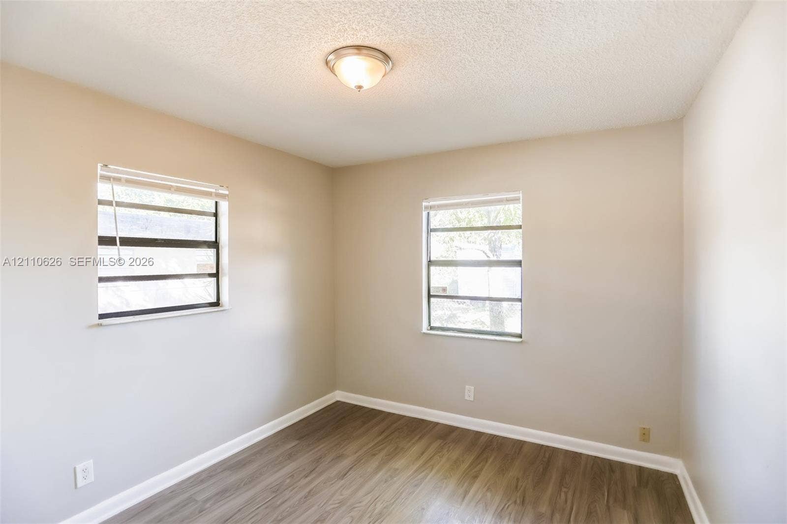 1301 NW 2nd Street, Dania, Dania Beach, FL 33004 Room featuring wood-finish flooring, neutral wall paint, two windows with horizontal blinds, and a centered flush-mount ceiling light