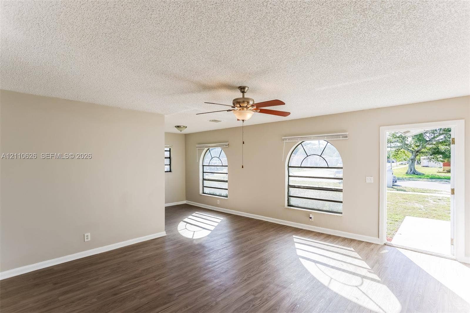 1301 NW 2nd Street, Dania, Dania Beach, FL 33004 Interior room featuring wood-finish flooring, two arched windows with grid detailing, and a central ceiling fan with integrated lighting