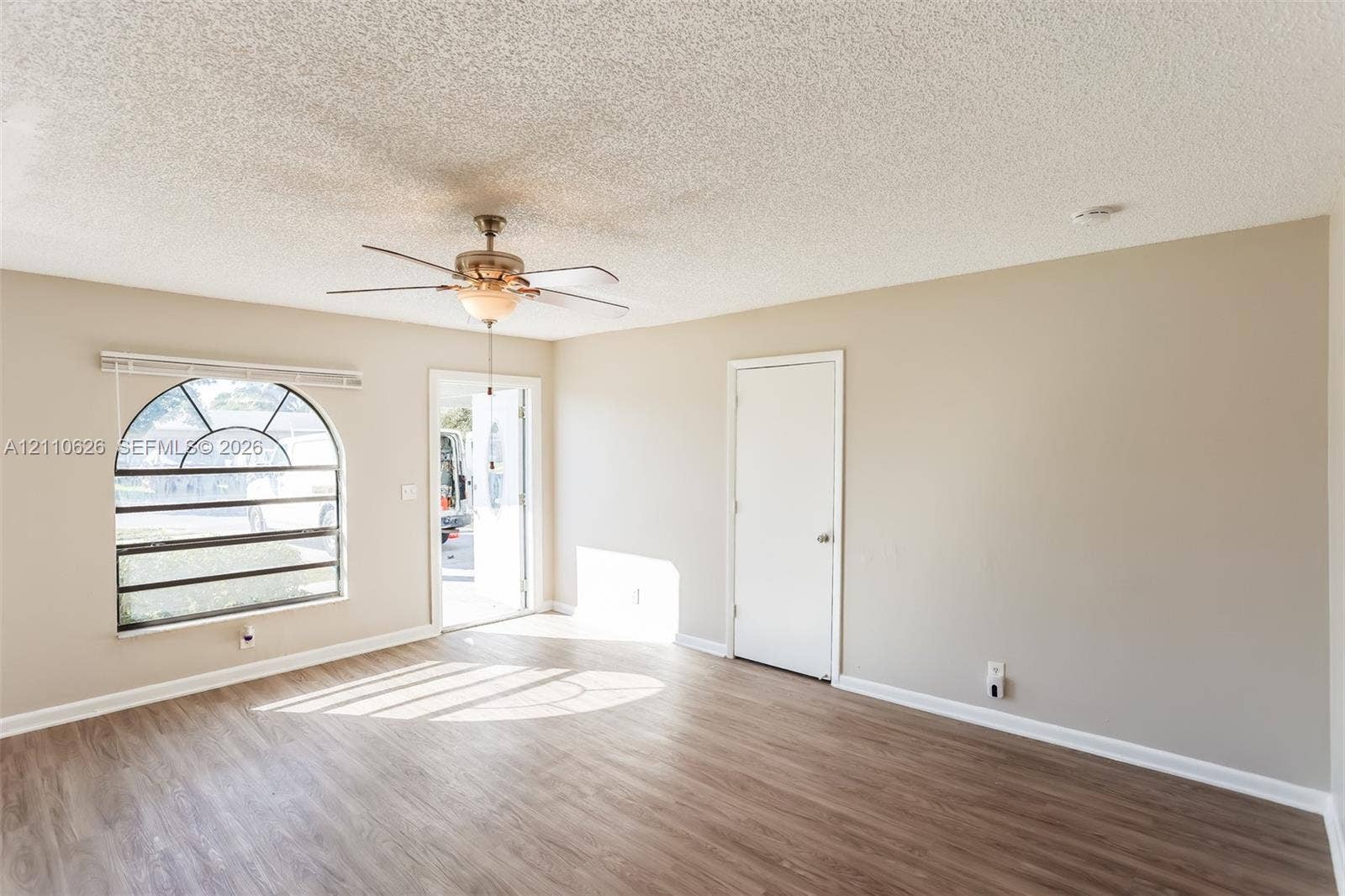 1301 NW 2nd Street, Dania, Dania Beach, FL 33004 Interior space featuring wood-finish flooring, an arched window, a ceiling fan with light fixture, and neutral-toned walls