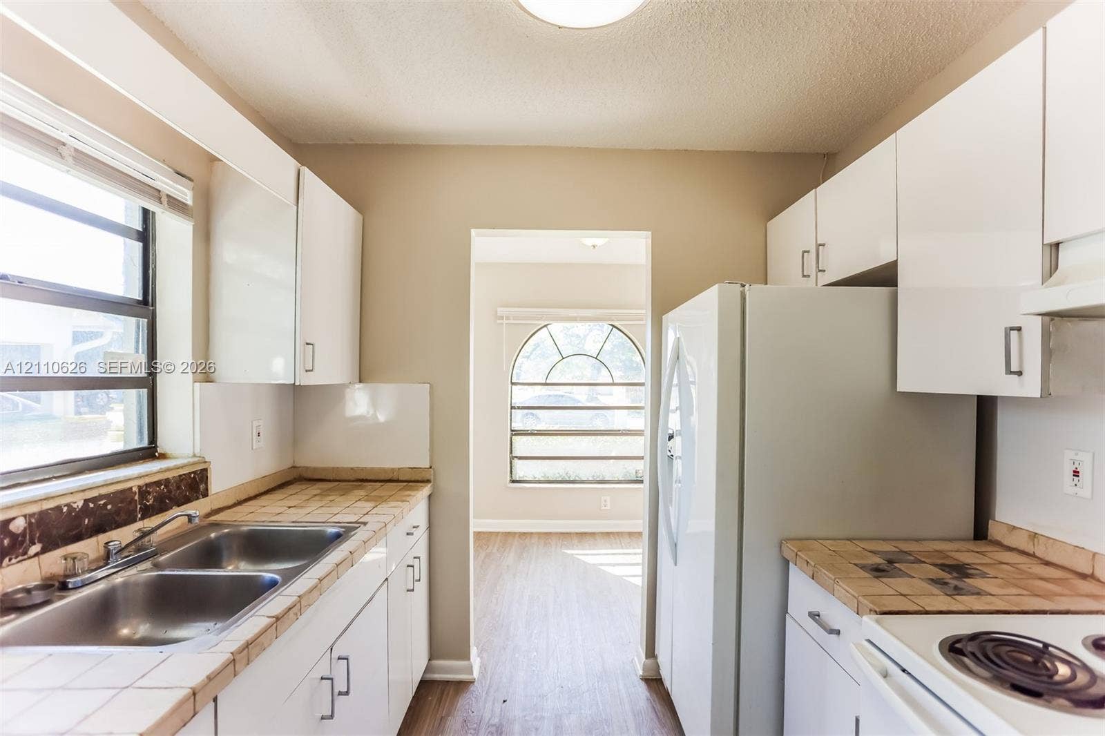 1301 NW 2nd Street, Dania, Dania Beach, FL 33004 Kitchen featuring white cabinetry, tile countertops, a double-basin stainless steel sink, and an arched window