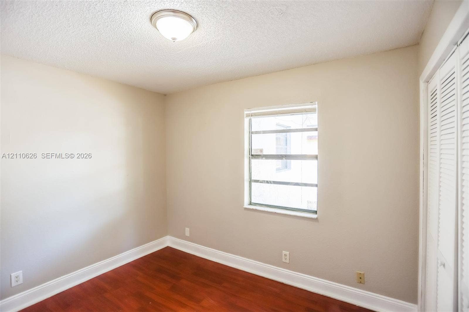1301 NW 2nd Street, Dania, Dania Beach, FL 33004 Room featuring wood-finish flooring, neutral wall paint, a single-pane window, flush-mount ceiling lighting, and louvered bifold closet doors