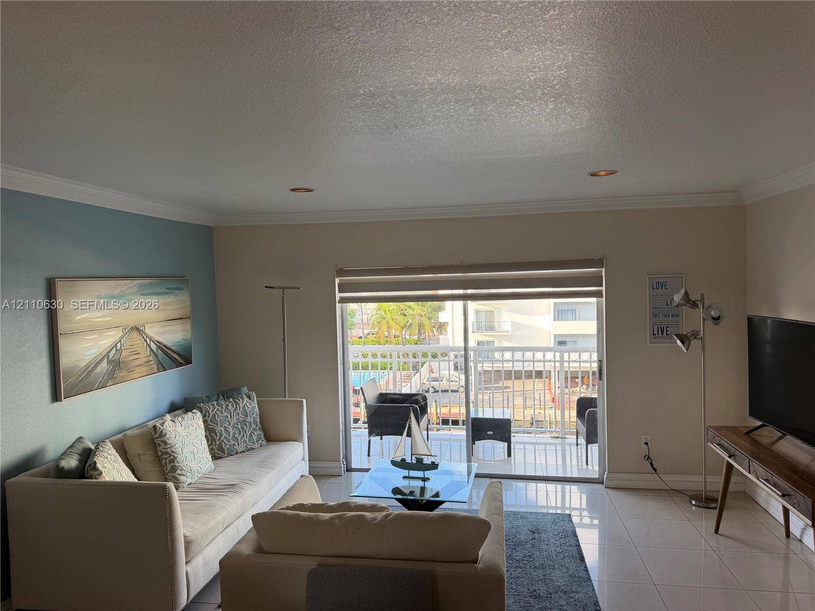 3601 NE 170th Street, #407, North Miami Beach, FL 33160 Living space featuring large-format tile flooring, crown molding, recessed lighting, and a sliding glass door providing access to a private balcony