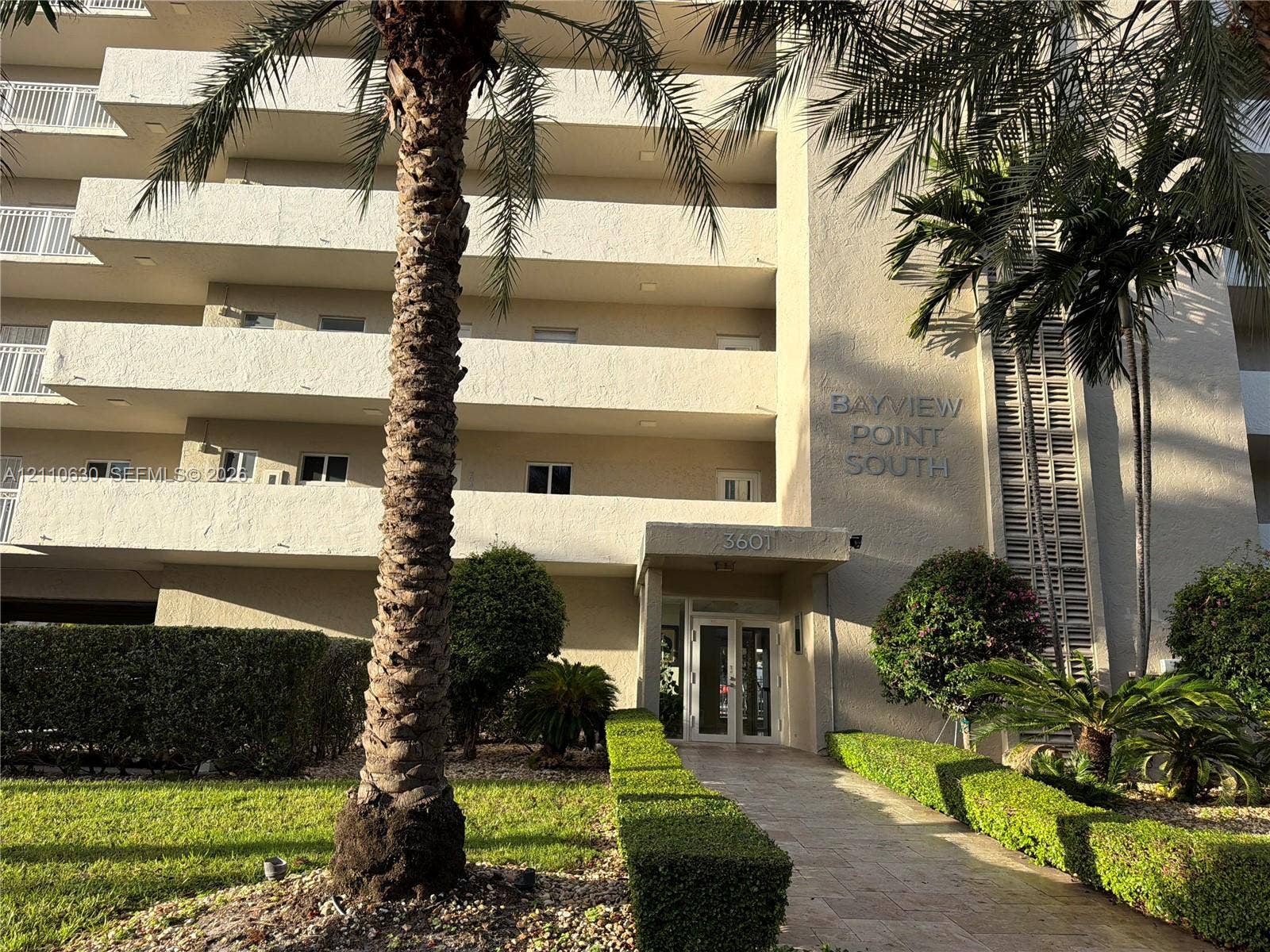 3601 NE 170th Street, #407, North Miami Beach, FL 33160 Multi-story stucco exterior featuring private recessed balconies, a covered entryway, and mature palm tree landscaping