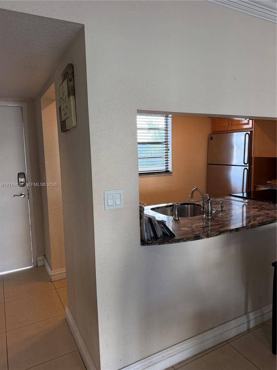 3601 NE 170th Street, #407, North Miami Beach, FL 33160 Kitchen pass-through featuring a stone-surface countertop, stainless steel sink with a high-arch faucet, and tile flooring