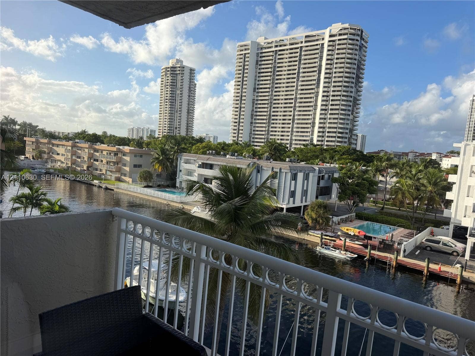 3601 NE 170th Street, #407, North Miami Beach, FL 33160 Private balcony with white metal railings overlooking a canal, watercraft, and dense palm tree foliage
