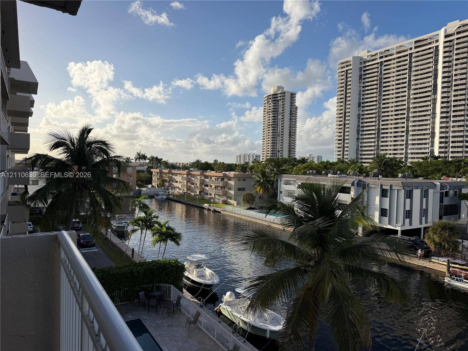3601 NE 170th Street, #407, North Miami Beach, FL 33160 Elevated balcony with a metal railing overlooking a canal, featuring tropical palm trees and direct water access