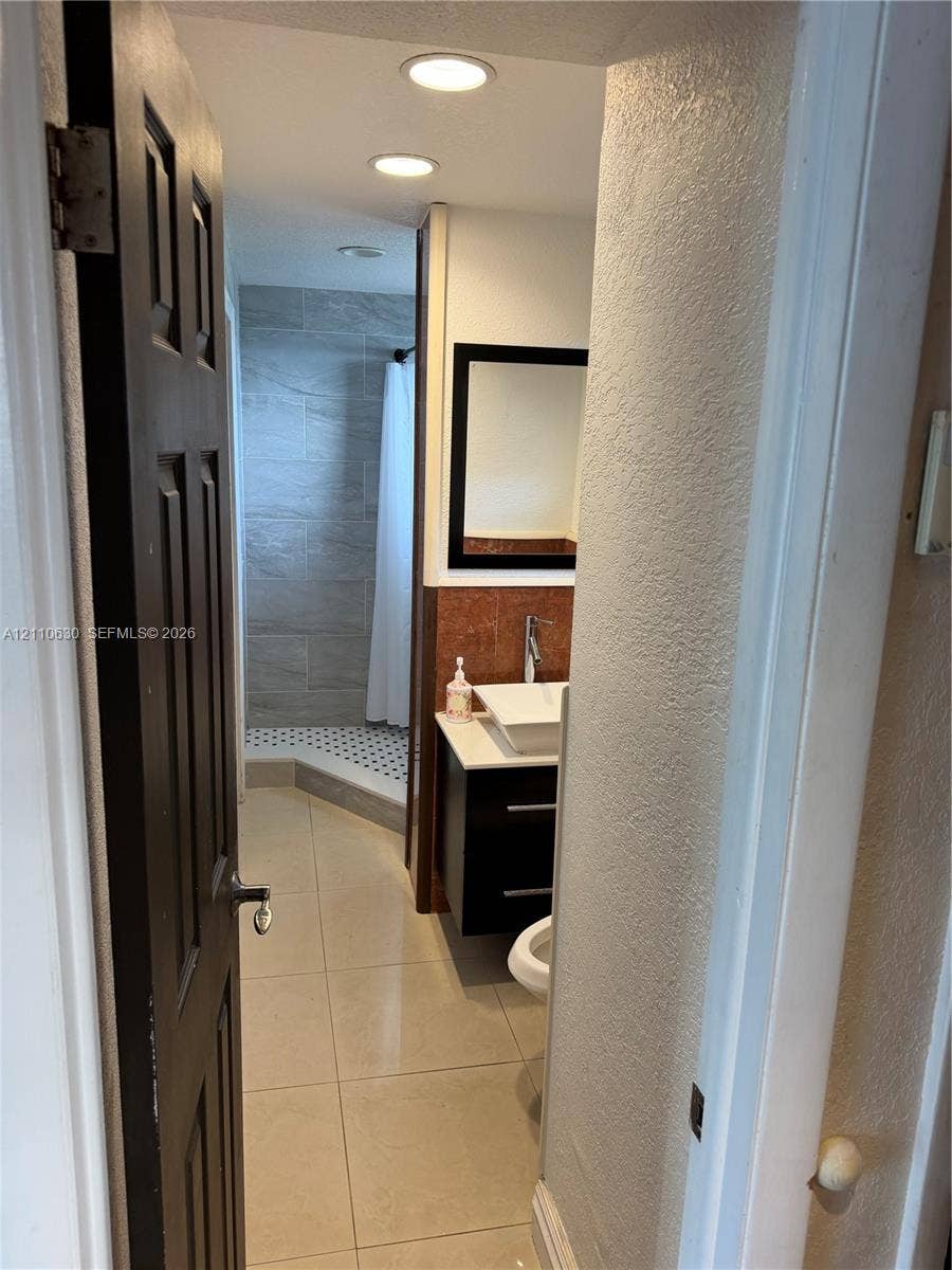 3601 NE 170th Street, #407, North Miami Beach, FL 33160 Bathroom featuring large-format floor tiling, a floating vanity with a rectangular vessel sink, integrated recessed lighting, and a walk-in shower with stone-style wall tile and geometric floor tile