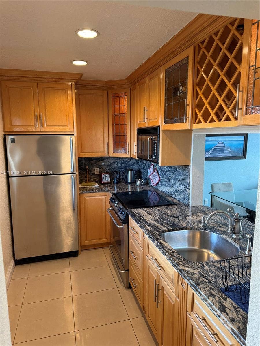 3601 NE 170th Street, #407, North Miami Beach, FL 33160 Kitchen featuring wood cabinetry with built-in wine storage, natural stone countertops, stainless steel appliances, and tile flooring