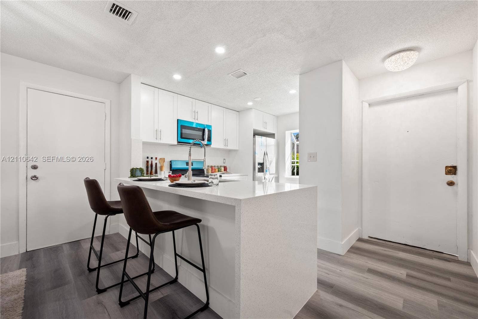 14732 SW 90th Terrace, Miami, FL 33196 Kitchen featuring white cabinetry, stone-surface breakfast bar with waterfall edge, wood-finish flooring, and stainless steel appliances