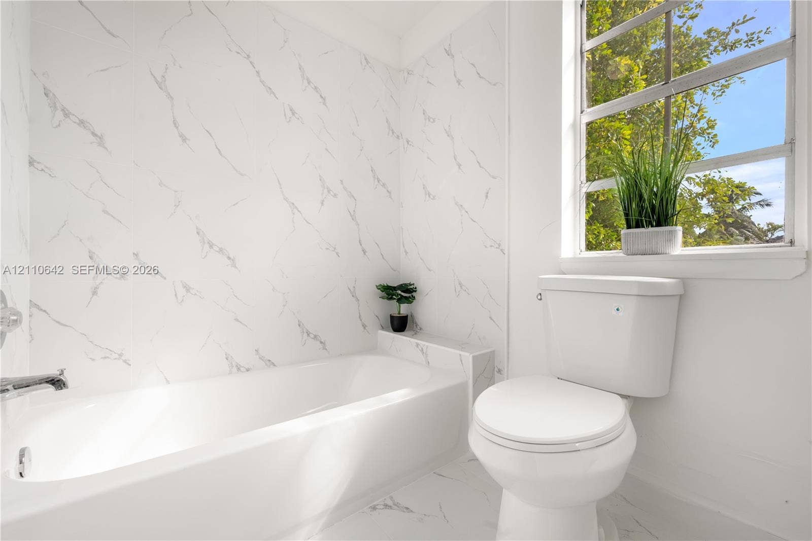 14732 SW 90th Terrace, Miami, FL 33196 Full-height stone-patterned tile wall surround, integrated bathtub with polished chrome fixtures, white ceramic toilet, and large window with exterior greenery